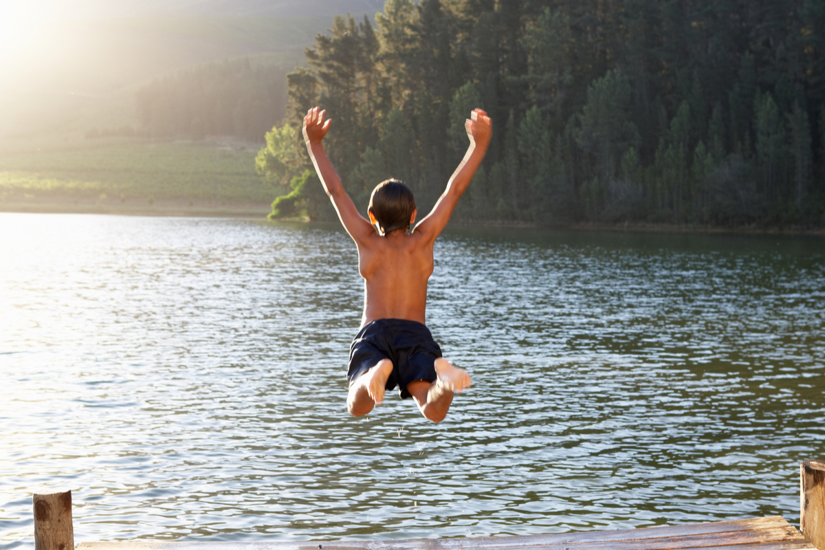 Bub springt vom Badesteg ins Wasser