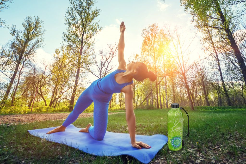 Young woman doing yoga exercises in the summer city park.