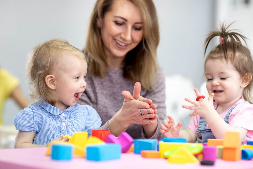 Cute woman and kids girls with play clay toys at day care center