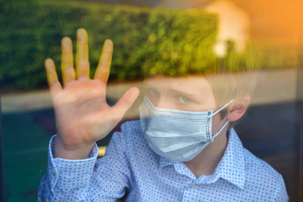 Young,Ill,Boy,Looking,Sad,With,Protective,Mask,At,Home