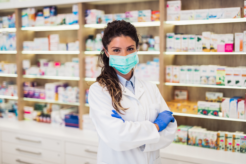 Female,Pharmacist,With,Protective,Mask,On,Her,Face,Working,At