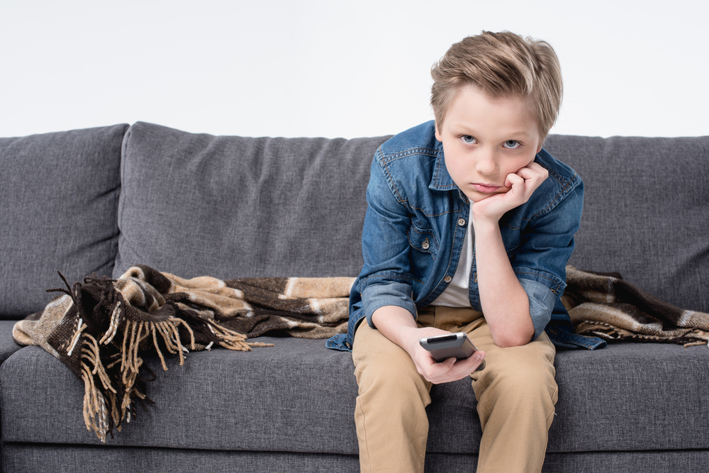 Pre-adolescent,Bored,Kid,Boy,Sitting,On,Sofa,And,Using,Remote