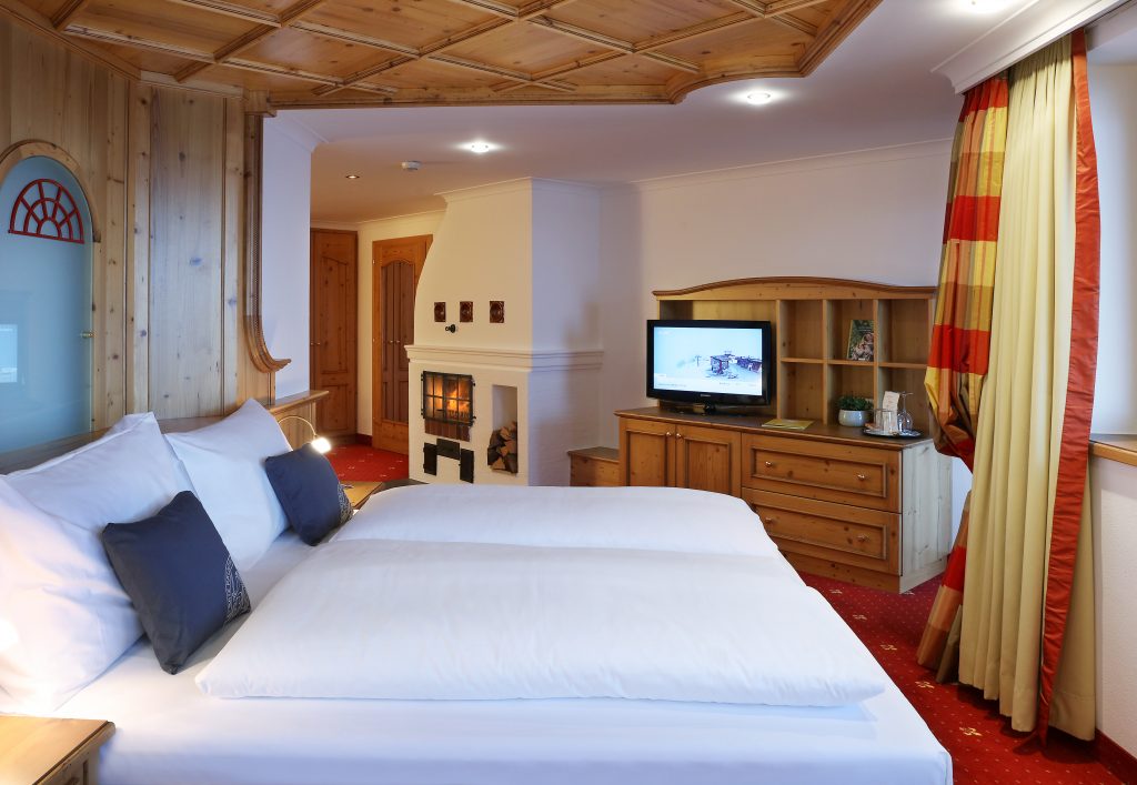 Sie sehen ein Doppelbett in einem Doppelzimmer Superior im JUFA Alpenhotel Saalbach**** mit TV. JUFA Hotels bietet erholsamen Familienurlaub und einen unvergesslichen Winterurlaub.