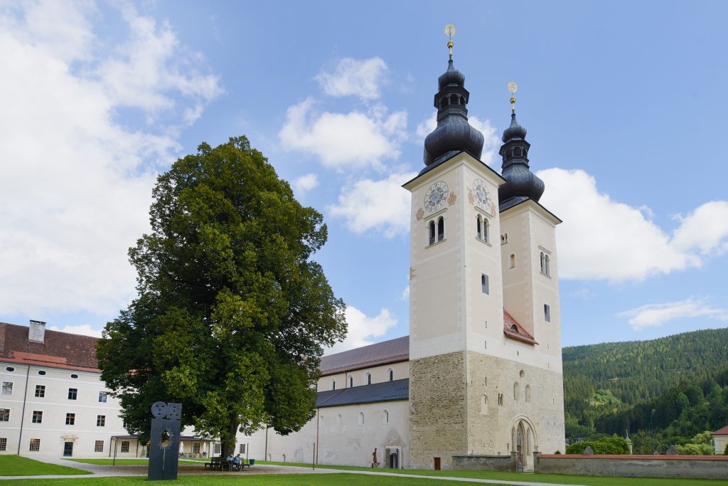 Sie sehen eine Aussenansicht mit Baum vom JUFA Hotel Stift Gurk im Sommer. JUFA Hotels bietet Ihnen den Ort für erlebnisreichen Natururlaub für die ganze Familie.