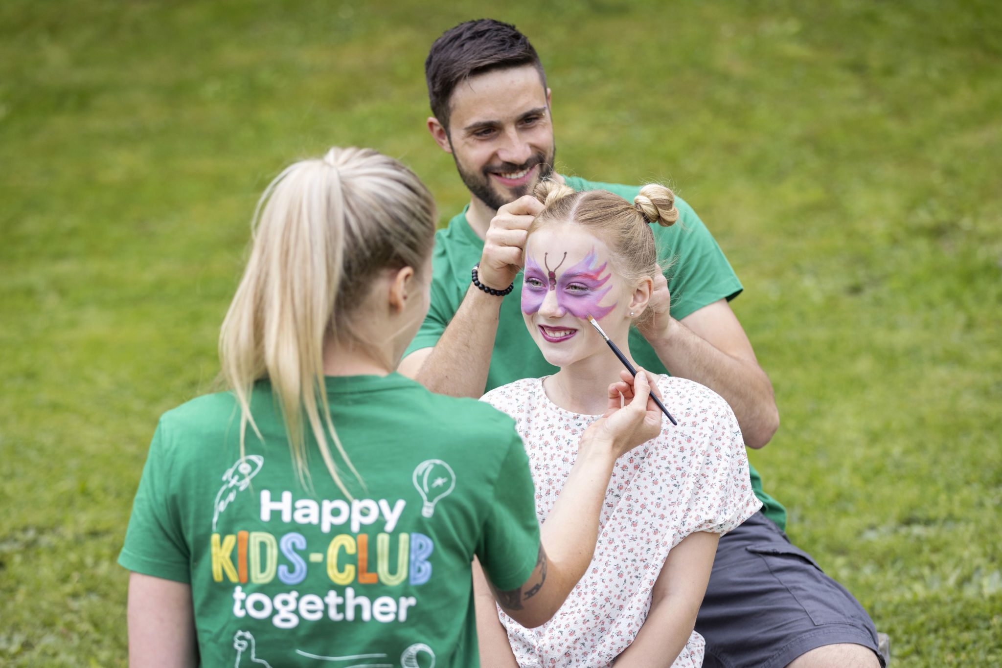 Sie sehen ein Mädchen, das von einem Kids-Club Betreuer der JUFA Hotels geschminkt wird. IHr werden auch die Haare gemacht.