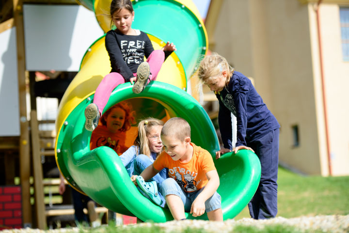 Kinder rutschen auf einem Spielplatz beim JUFA Hotel Neutal - Landerlebnis. Der Ort für erlebnisreichen Natururlaub für die ganze Familie.