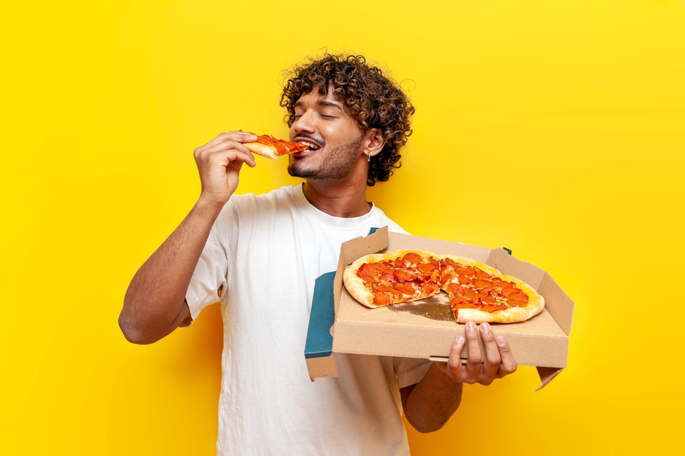 Young,Indian,Man,Eating,Delicious,Pizza,On,Yellow,Isolated,Background,