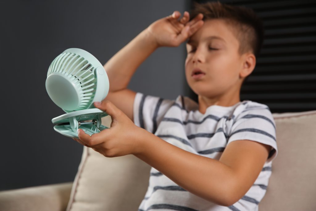 Little,Boy,With,Portable,Fan,Suffering,From,Heat,At,Home,