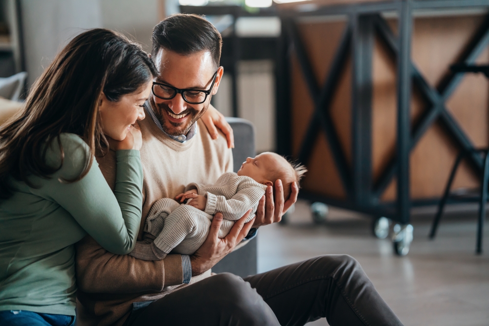 Smiling,Mother,And,Father,Holding,Their,Newborn,Baby,Daughter,At