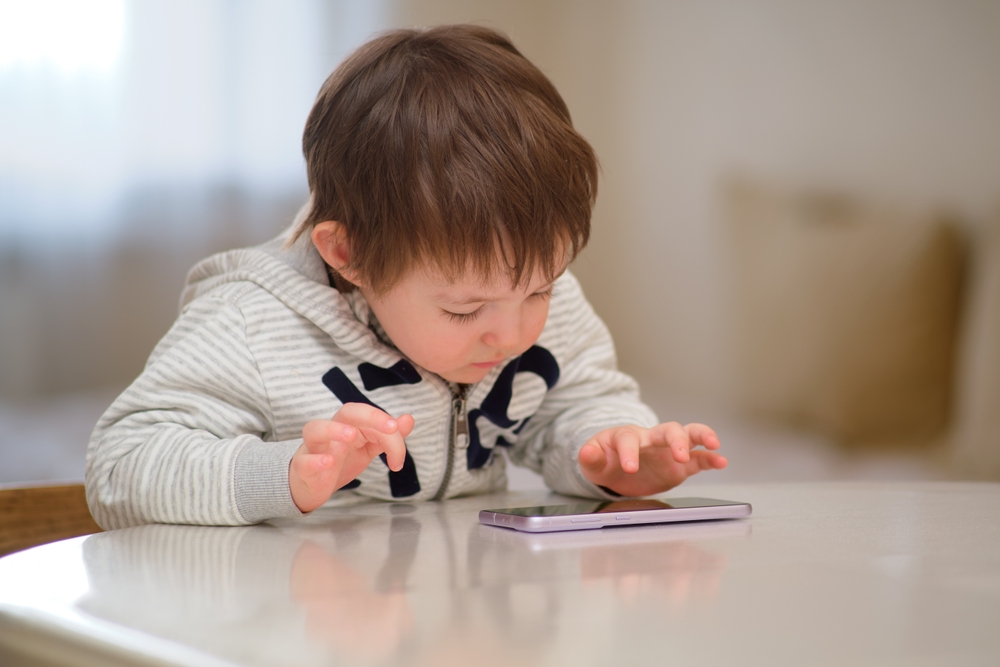 Pensive,Baby,Plays,With,A,Mobile,Phone,While,Sitting,At