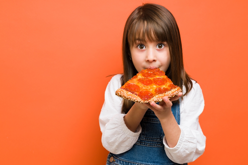 Adorable,Little,Girl,Biting,A,Slice,Of,Pizza,And,Enjoying